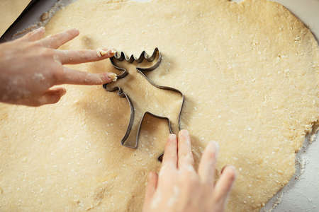 Closeup of child hands cutting cookies from dough. Boy in apron pressing cookie cutter elk shape. baking christmas biscuits in home kitchen.の写真素材