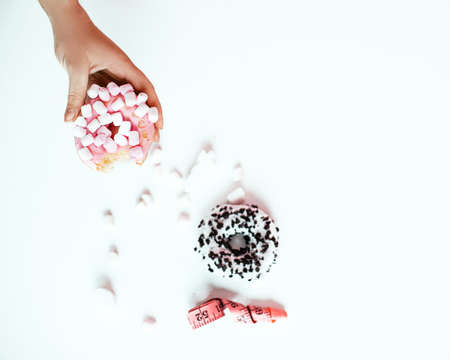 Female hands holding donut, measuring tape over white background. Top view, flat lay. Sweet, dessert, diet concept, copy space.の写真素材