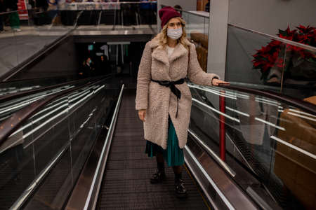 young blond woman in artificial fur coat and hat climbs on excavator in shopping center in medical...
