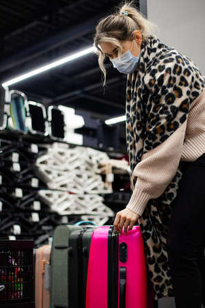 Pretty woman in casual clothes, mask and leopard scarf is trying locks in bright pink suitcase in department of bags in supermarket. Trips to pandemic. Shopping.Active lifestyle. Christmas holidays.の写真素材