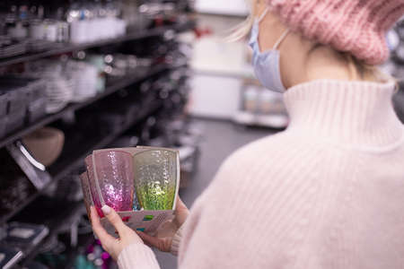 Masked customer in tableware department at mall is looking at set of multicolored glass circles as gift forNew Year. New normal concept. Concept of shopping for home. New Year's shopping. Lifestyle.の写真素材