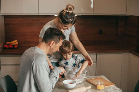 Dad and Mom arranged. Joint baking hours for little boy, 4 - 5 years old. Bake cookies in kitchen at home. Teamwork. Combining activities for young family. Happy working peopleの写真素材