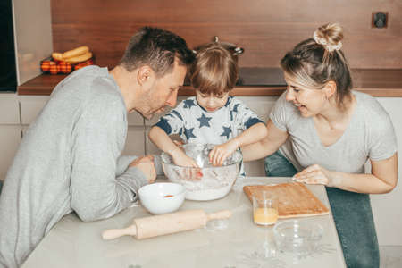 Young woman laughing while her men, father and son, cooking Cookies together. Prepare dough for...