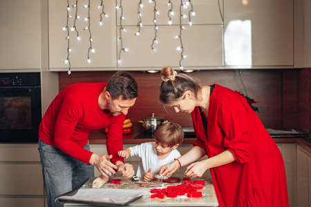 Happy evening on Christmas Eve or New Year's Eve, family of three person is busy baking cookies,...