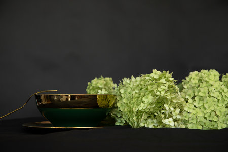Refined green dishes with gold border On black background. Serving with hydrangea flowers. High class, elegance. Copy space.の写真素材