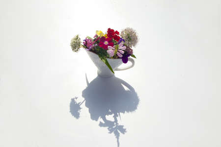 Bouquet of different vibrant colors flowers in vase on white background, play of lights and shadows on table, summer day light, natural flower decor, top viewの写真素材