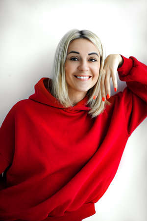 Front view of positive smiling pretty young white woman in colorful bright red hooded sweatshirt and bright red manicure looking at cameraの写真素材