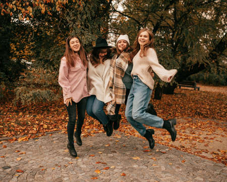 Young fair-haired and dark-haired women friends, two of them having hats on their heads, dressed in...