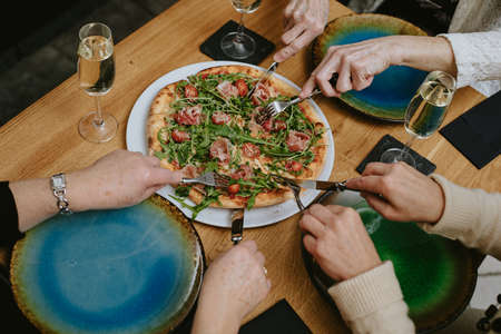 Top view of hands with thin fingers of unrecognizable elderly people possibly women eating pizza...