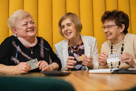 Laughing elderly women having pills in their hands and calculator on table, dicussing medicine,...