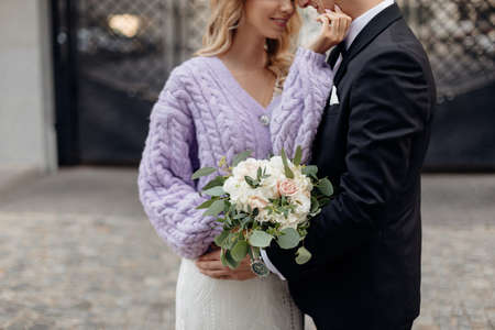 Crop photo of blonde bride with curly hair in white wedding dress and lilac jacket having bouquet in...
