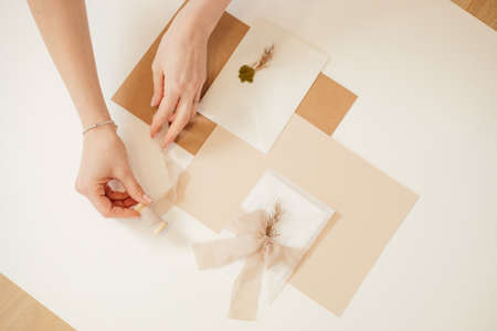 Cropped photo woman hand, peach composition paper envelopes, ribbons, tape reel, wax, cut out handmade jobbing.の写真素材