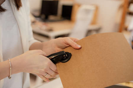 Cropped photo woman hands hold using cutting out stapler dense cardboard, atach equipment chancellery tool. Close upの写真素材
