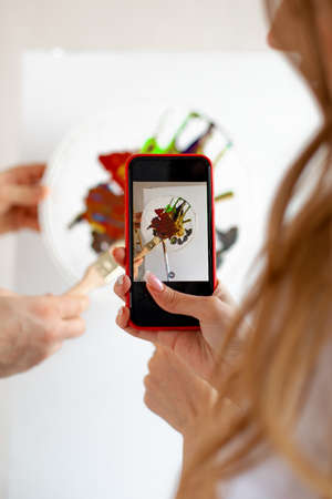 Unrecognizable woman with long hair taking photo of watercolor palette with brushes on blank canvas by mobile phone.の写真素材