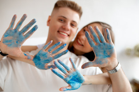 Happy smiling young couple of pretty woman stand behind man in white T-shirts showing hands covered with blue paint.の写真素材