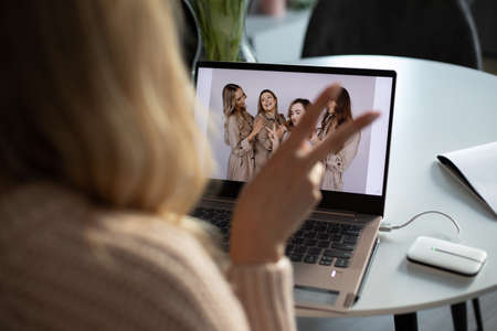 Portrait of young blonde smiling woman celebrating promotion at home. Show victory. Holiday on distance. Laptop on deskの写真素材