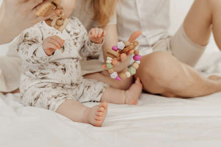 Cropped view of family with plump infant baby toddler holding modern wooden eco-friendly teether...