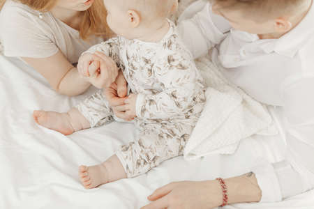 Top view of young family in white clothes sitting on white cotton bed linen with cute little blue-eyed baby infant.の写真素材