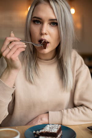 Vertical image of serious attractive blond woman, looking at camera, trying powdered sugar dessert food, chocolate forkの写真素材