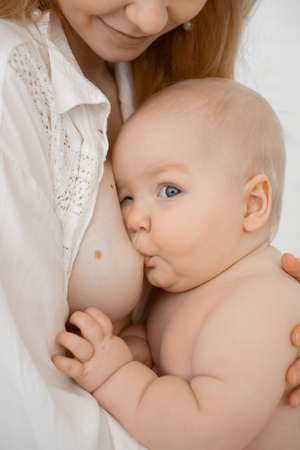 Vertical cropped of bare woman with small baby eating, breastfeeding, mother nursing newborn. Nipple...