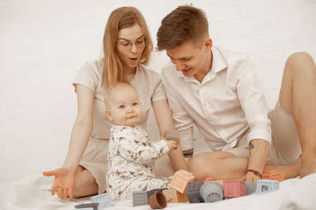 Happy curious family, woman in glasses, man, baby playing games shapes, cubes. Spending time,...