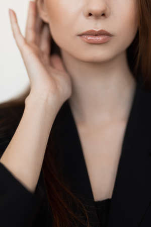 Cropped photo of young slim woman model with long dark hair, make-up wear black blazer touching ears, titivating hair.の写真素材