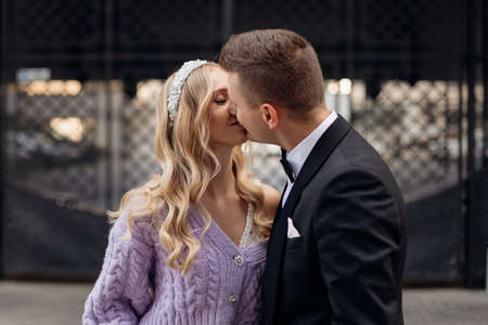 Beautiful couple of bride with long wavy fair hair in bridal dress, lilac cardigan with bandeau on head and bridegroom.の写真素材