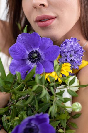 Portrait of beautiful lady covering bare breast with bouquet of bright wildflowers. Attractive woman with perfect makeup and natural accessory. Fashion photo, posing on white background in studioの写真素材