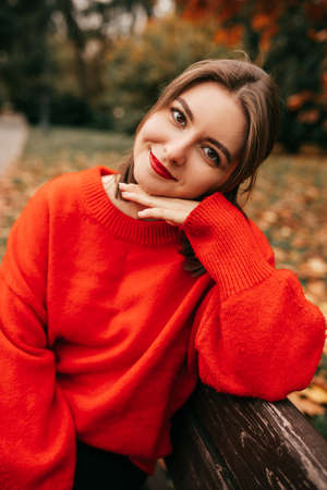 Vertical pretty beautiful woman, leaning on hand, sitting on wood bench in autumn park. Relaxing, contemplating natureの写真素材