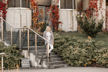 Portrait of blond beauteous woman walking stone stairs holding railing, expression after tour park, near building museumの写真素材