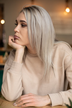 Portrait of young gorgeous pensive woman with long hair with make-up resting chin on hand, being...
