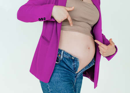 Unrecognizable pregnant woman in not buttoned denim pointing fingers at big belly, problems during pregnancyの写真素材