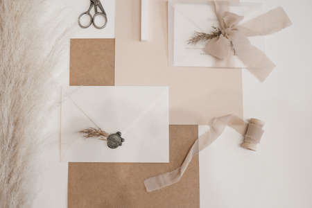 Top view of composition of sheets of paper, scissors, white envelope with grey wax seal, bow of...