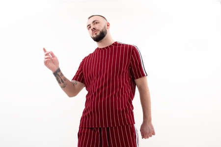 Portrait of young handsome bearded man with short dark hair wearing red striped sport wear, raising hand up, posing.の写真素材