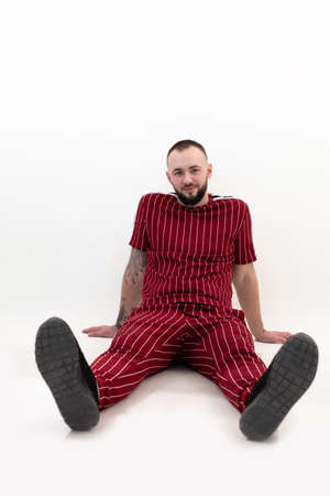 Portrait of young contented bearded man with short dark hair wearing red striped sport wear, sitting, leaning on hands.の写真素材