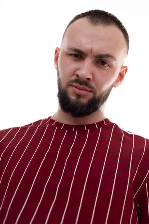 Portrait of young angry handsome bearded man with short dark hair wearing red striped sweatshirt,...