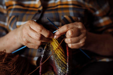 Unrecognizable woman hands of elderly woman, spoke knitting colorful checkered clothes. Making new scarf or sweaterの写真素材