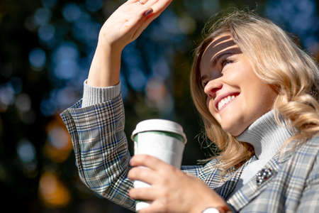 Smiling blonde in tweed jacket with cup of hot drink in his hands, he squints, closing his hand from...