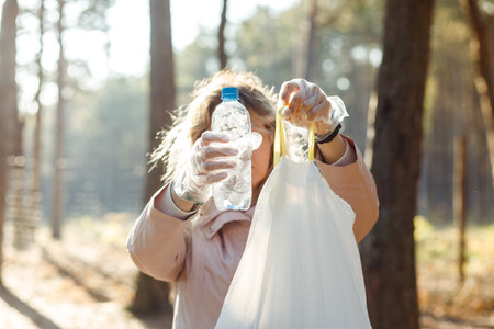 Woman activist and assistant showing bag full of rubbish to camera, helping clean forest from...