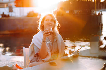 Portrait of young happy good-looking woman with long fair hair, wearing blue shirt, white sweater, sitting at table.の写真素材
