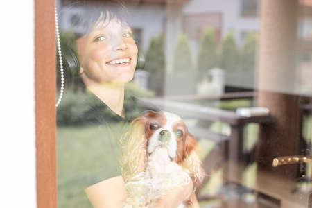 Portrait of smiling happy joyful teenager boy holding dog Cavalier King Charles spaniel, looking...