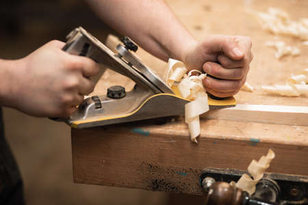 Close-up of cropped carpenter hands working with plane equipment tool on the workbench. Carpentry...