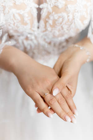 Closeup photo of elegant, shining gentle woman hands hold each other, bride with excellent manicure. White wedding dressの写真素材