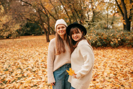 Female friendship. Portrait of autumn time in park among pile of fallen leaves of two happy young women standing embracing. Fun vacation. Weekend. Walking in fresh air.の写真素材