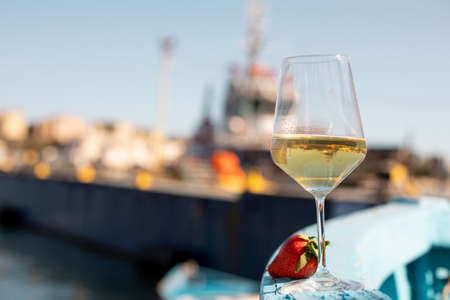 Composition of glass with white wine and strawberry putting on board of blue wooden boat on sunny day. Soft focus.の写真素材