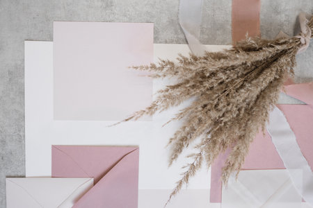 Top view of composition of colorful paper sheets, ribbons, white and pink envelopes, bouquet of dried pampas grass.の写真素材