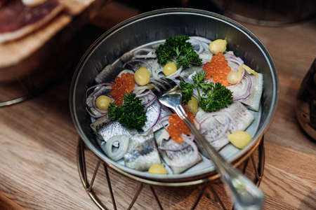 Serving bowl of fresh salty herring with red caviar, onion and green on stand closeup top view. Portion of seasonal appetizer from fish, nutritious dish. Food court, delicious meal, luxurious serviceの写真素材