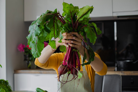 Blond woman hiding face behind bunch of beetroots with leaves, cook fresh organic salad in kitchen. Healthy eating, dietの写真素材
