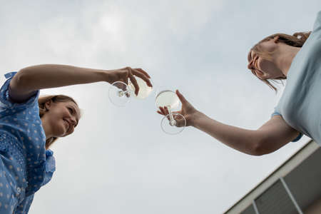 Happy young girls standing opposite each other, clinking glasses and drinking wine closeup from...