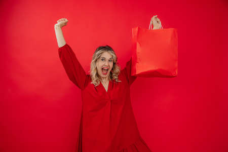 portrait of happy young cute blonde woman posing with shopping bags over Red background.